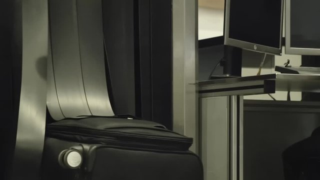 Baggage is inspected through an X-ray screen at airport checkpoint. female hand of passenger takes suitcase off conveyor after checking for prohibited items.