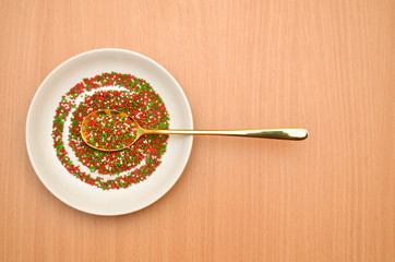 Round baking topping, sprinkle in a white saucer with a golden spoon on a wooden table, top view