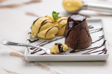 Petit gateau dessert; Petit gateau with vanilla ice cream and chocolate sauce in a white plate on white wooden background.