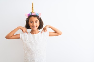 Beautiful child girl wearing unicorn diadem standing over isolated white background looking...