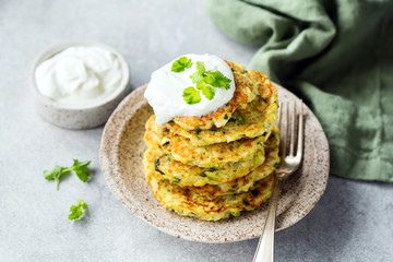 Vegetarian zucchini pancakes or fritters with sour cream stack on plate. Healthy appetizer or snack