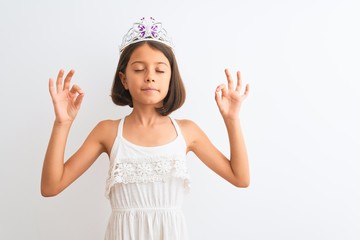 Obraz na płótnie Canvas Beautiful child girl wearing princess crown standing over isolated white background relax and smiling with eyes closed doing meditation gesture with fingers. Yoga concept.