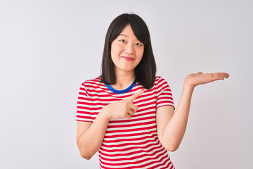 Young beautiful chinese woman wearing red striped t-shirt over isolated white background amazed and smiling to the camera while presenting with hand and pointing with finger.