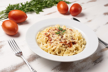 Fettuccine pasta with tomato sauce, parsley and basil in a white plate on a rustic wooden table background, soft light