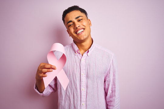Young brazilian man holding cancer ribbon standing over isolated pink background with a happy face standing and smiling with a confident smile showing teeth