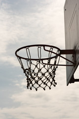 Closeup of a basketball hoop, basket with white net and blue sky with clouds in background