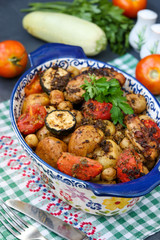Chicken thighs baked with potatoes, tomatoes and zucchini, located in ceramic form, on a dark background, vertical orientation