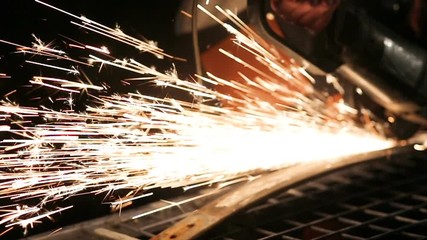 Bearded mechanic cuts metal with an angle grinder in a service station - Powered by Adobe