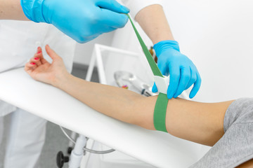 the nurse in the clinic tightens the harness on the hand of a young girl to take blood from a vein for analysis