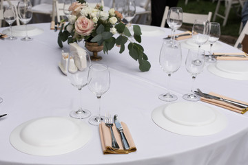 Wedding table setting decorated with fresh flowers in a brass vase. Wedding floristry. Banquet table for guests outdoors with a view of green nature. Bouquet with roses, eustoma and eucalyptus leaves