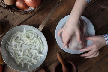manos de una mujer cogiendo un pollo crudo sobre una mesa llena de ingredientes mientras prepara la comida 