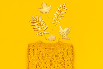 Autumn flat lay composition. Orange yellow knitted woolen female sweater and golden leaves on yellow background top view. Fashionable women's fall accessories. Cozy Knit Jumper Stylish Lady Clothes