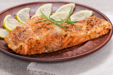 Grilled salmon with spices, lemon and rosemary, on a clay plate.