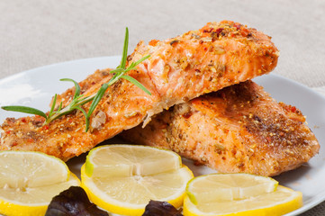 Grilled salmon with spices, lemon and basil, on a light plate.