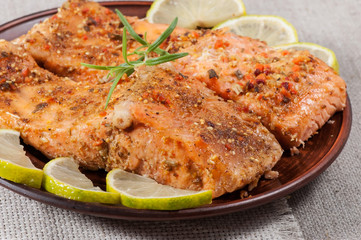 Grilled salmon with spices, lemon and rosemary, on a clay plate.