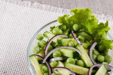Salad of cucumber and green sweet peas with onions and herbs in a glass plate.