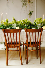Wedding table with chairs and plates, forks, spoons, knifes on cloth decorated with greenery bouqet