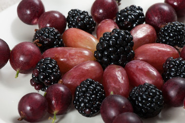 Fresh sweet fruits grapes, blackberries and gooseberries on a light plate.