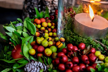 Hugge-style autumn decoration with a burning candle. Home decoration with red berries and small decorative apples.