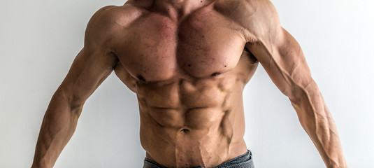 Fototapeta na wymiar Bodybuilder flexing his muscles in studio. The torso of attractive male body builder on white background.