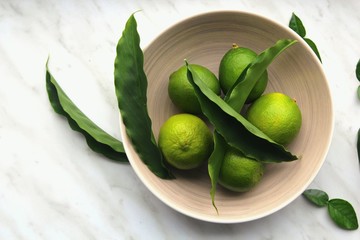 vista desde arriba de limas frescas junto con hojas verdes sobre un plato marrón en una mesa de mármol
