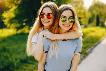 Fototapeta premium two beautiful young beautiful girls with shiny blond hair and a skirt and walk and spend goood time in a sunny summer park