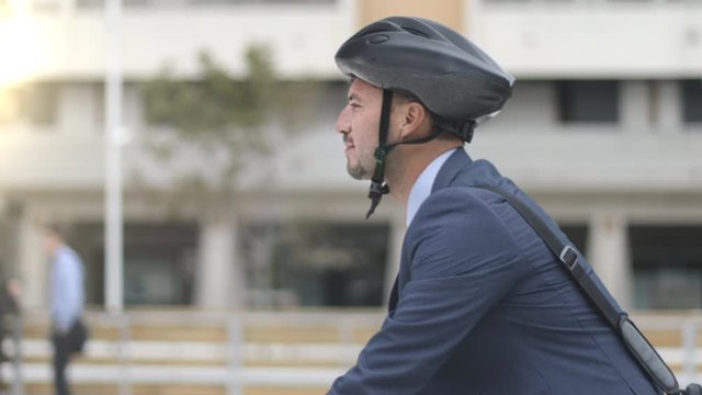 Amazing portrait of handsome young businessman with a briefcase on the shoulder and bike helmet riding his bike in the city. Tracking shot.