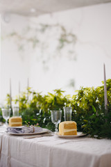 Wedding table with chairs and plates, forks, spoons, knifes on cloth decorated with greenery bouqet