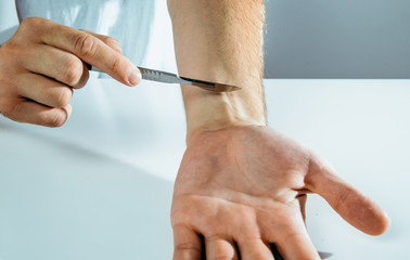The man cuts his skin with a scalpel. Suicide concept, treatment attempts. Using sharp tools on the skin. Vein cutting.