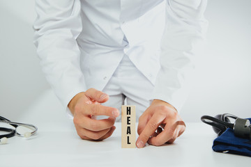 The doctor holds a block with the word HEAL in his hand. Medical and pharmaceutical concept. A man wearing a white coat and stethoscope heals.