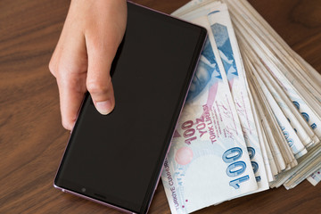 the woman use mobile phone, open apps ,shopping is easy with technology have a lot of Turkish money on the table.