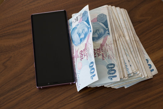 the woman use mobile phone, open apps ,shopping is easy with technology have a lot of Turkish money on the table.