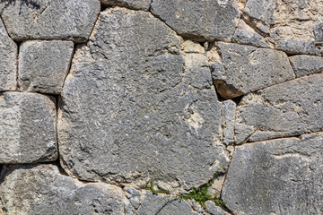 The ancient megalithic walls surround the acropolis of Amelia, in Umbria, Italy. Texture composed ofirregular huge blocks of stone. The grass grows between the interstices of the wall.