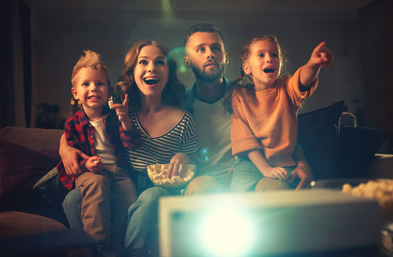 family mother father and children watching projector, TV, movies with popcorn in   evening   at home.