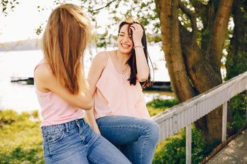 two beautiful and bright friends in pink t-shirts and blue jeans walking in the sunny summer park
