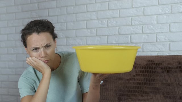 Water from the ceiling. A sad woman walks in the room and holds a tah into which water is dripping from the ceiling.