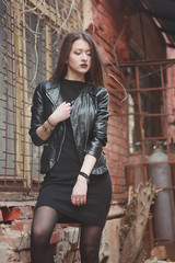 Woman wear on a leather jacket, black dress and tights in grunge gothic style outdoors