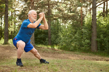 Portrait of healthy active elderly male pensioner in running shoes exercising outdoors, holding...