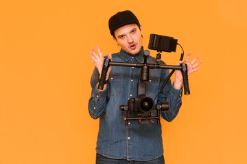 Guy in a blue t-shirt having fun and holding stabilizer for cameras near the orange background