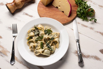 Homemade tortellini with butter and sage in a white plate on white wooden table background. Soft light