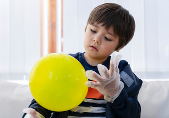 Cute boy wearing disposable protective plastic glove and holding yellow balloon,Kid preparing...