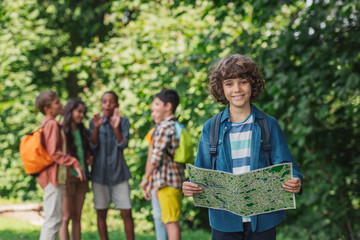 selective focus of happy and curly boy holding map near friends
