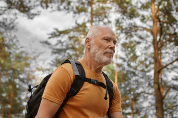 Close up image of happy bearded Caucasian male traveler backpacking alone, having energetic look. Stylish active man backpacker hiking with rucksack, enjoying healthy lifestyle and cardio activity