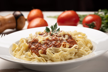 Pasta Fettuccine Bolognese with tomato sauce in a white plate on rustic wooden table background, soft light
