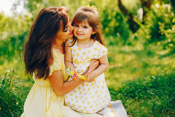 in a summer solar park near green trees, mom walks in a yellow dress and her little pretty girl