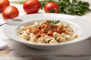 Italian tortellini (capeletti, agnolini) with tomato sauce in a white plate on rustic white wooden table background
