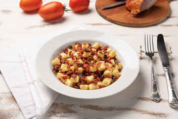 Homemade italian gnocchi with dry tomato, bacon and parmesan cheese in a white plate on white wooden table.  Soft light