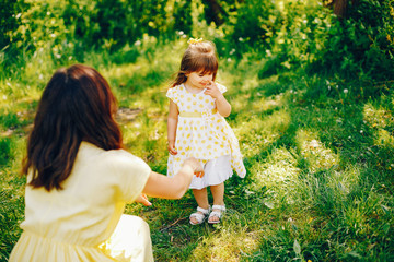 in a summer solar park near green trees, mom walks in a yellow dress and her little pretty girl