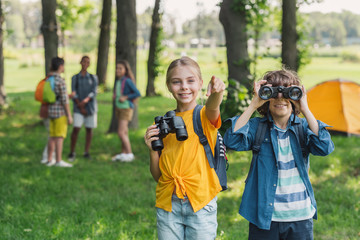 Selective focus of kid looking through binoculars near friend pointing with finger