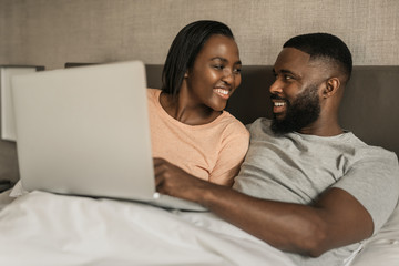 Fototapeta premium Smiling African American couple using a digital tablet in bed